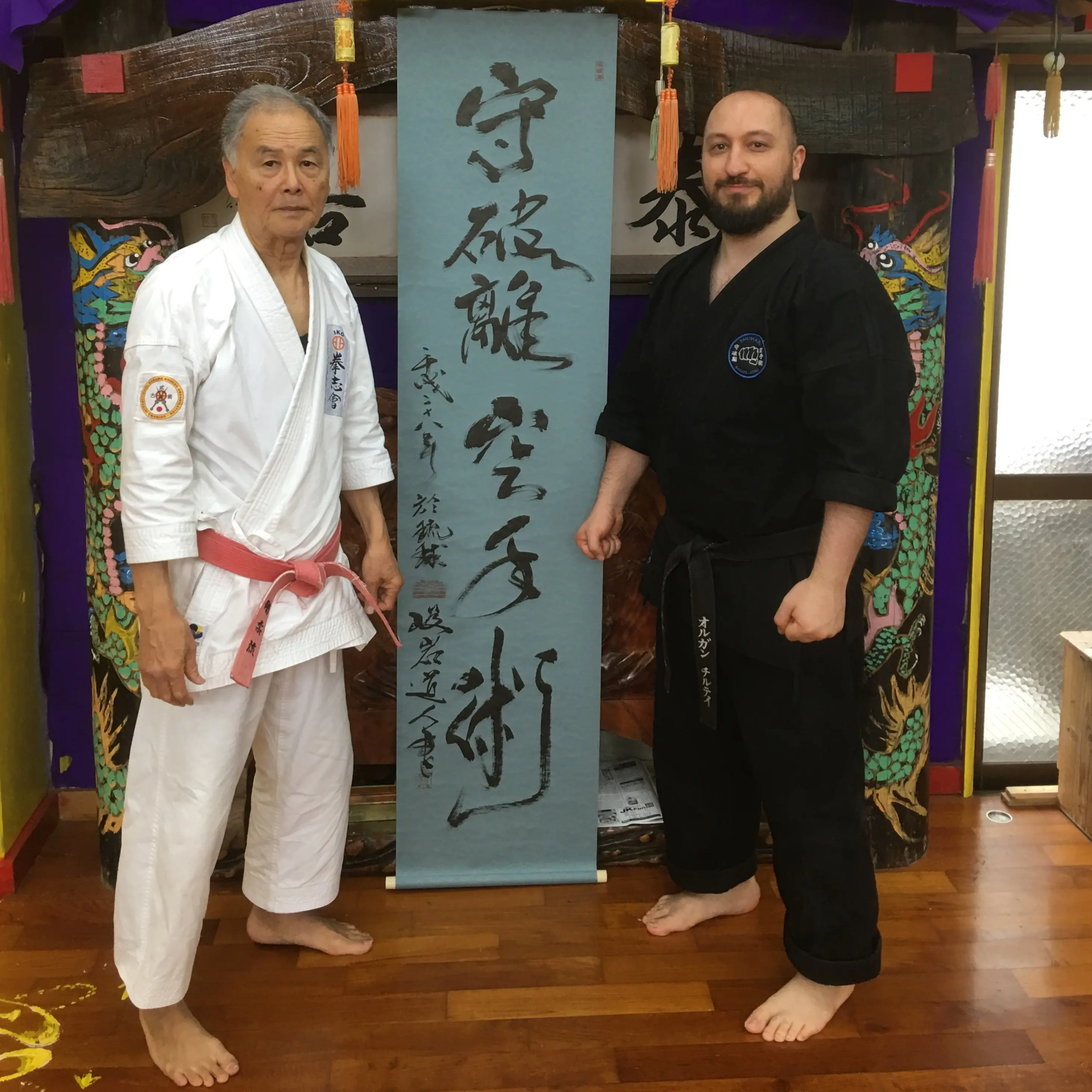Olgun Tiltay in Okinawa in front of Shuhari Karate-Jutsu banner written by Hokama Sensei [10th Dan] Gojuryu Karate